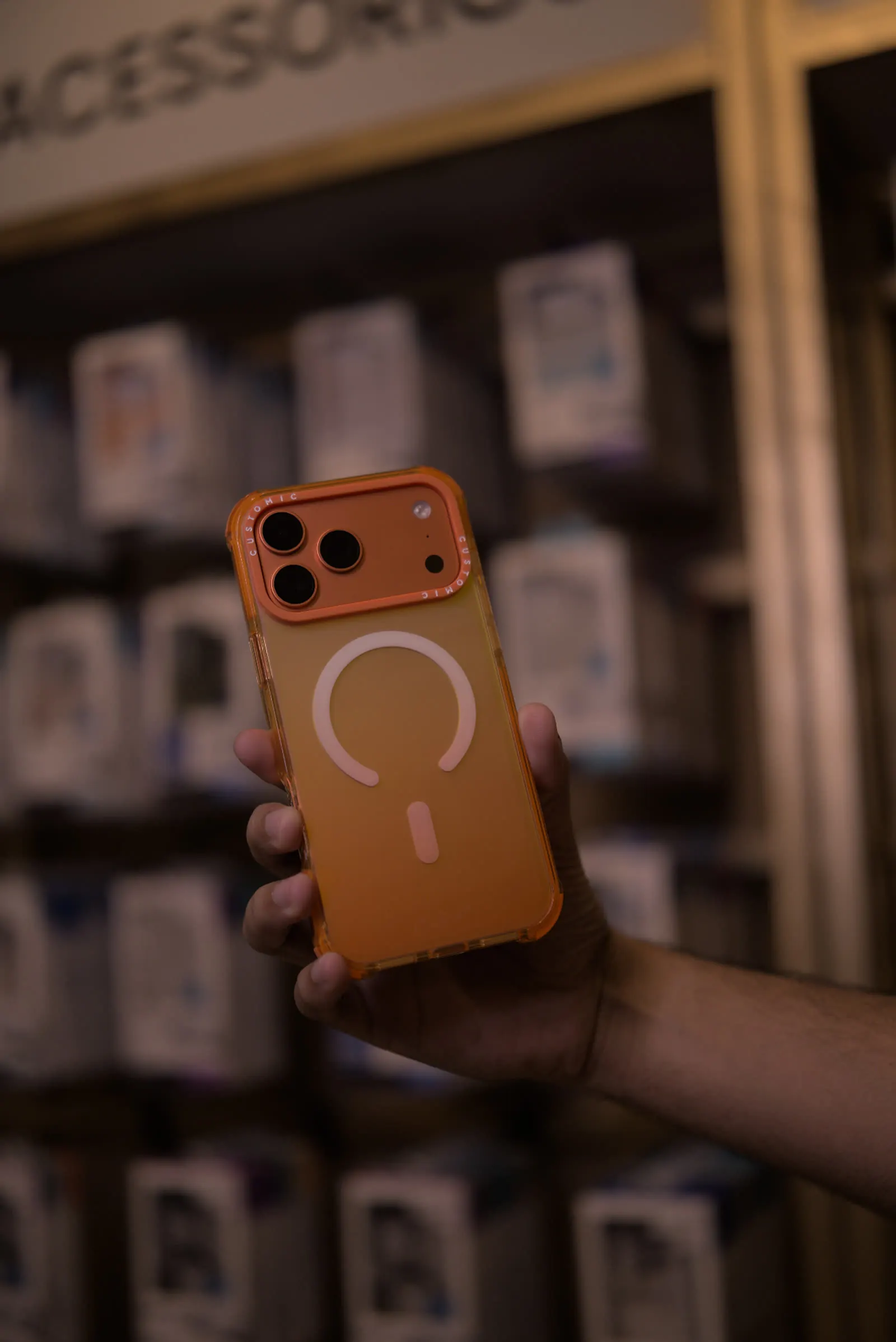 Capinha laranja translúcida com MagSafe à frente da parede de acessórios da Manoceo.